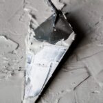 Close-up van een troffel die natte cementmortel gladstrijkt op een muur, met focus op de textuur.