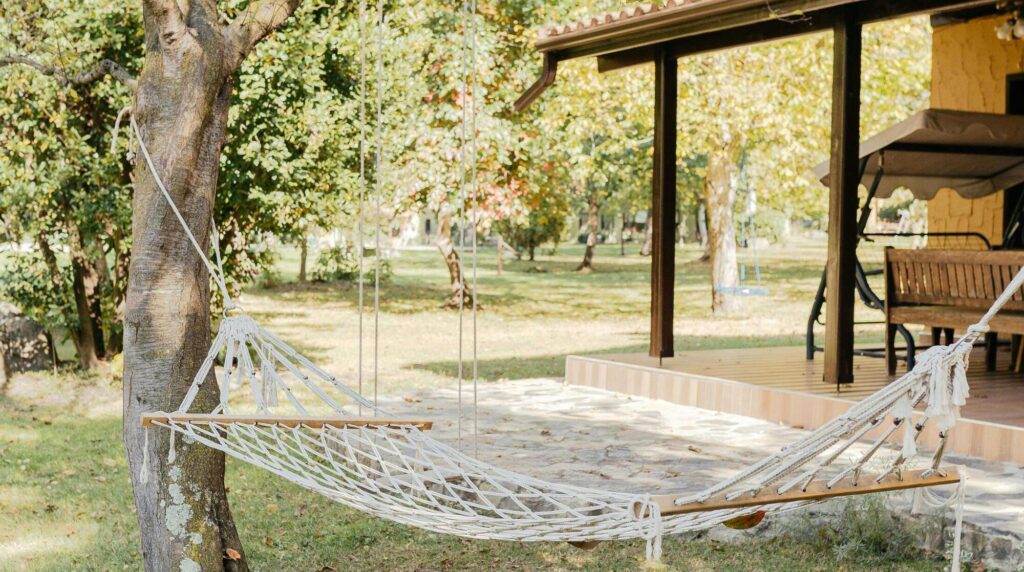 Hangmat hangt onder overkapping in tuin met bomen op de achtergrond
